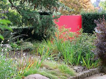 Hier sorgt ein Sichtschutzelement aus farbigem Acrylglas für ein optisches Highlight in einer Eibenhecke.